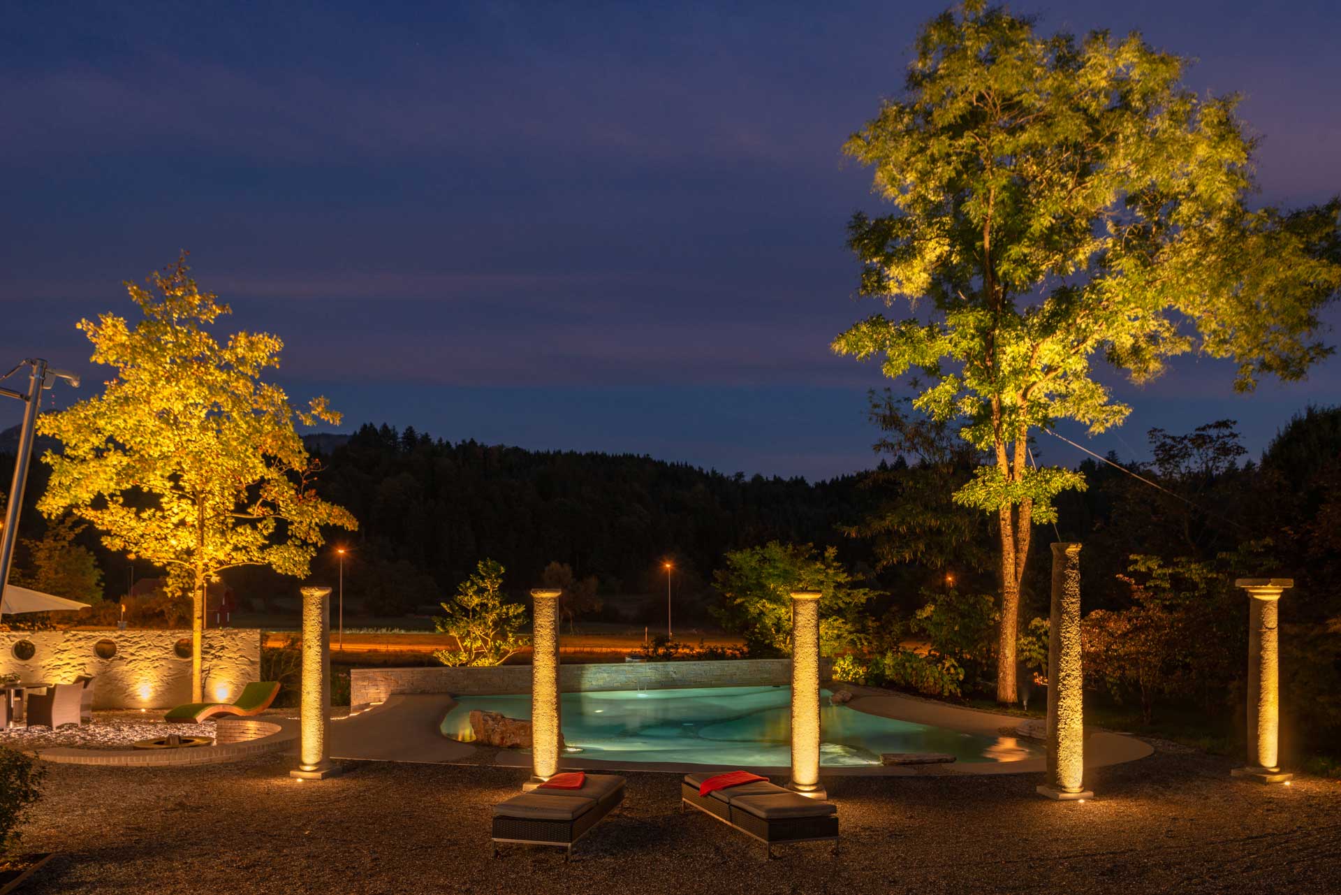 Garten mit südlichem Flair, Säulen sind mit Superspot beleuchtet, ein mit Gigaspot beleuchteter Pool im Hintergrund